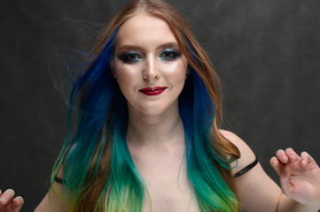 Portrait of caucasian cute model with long colored hair and makeup on gray background