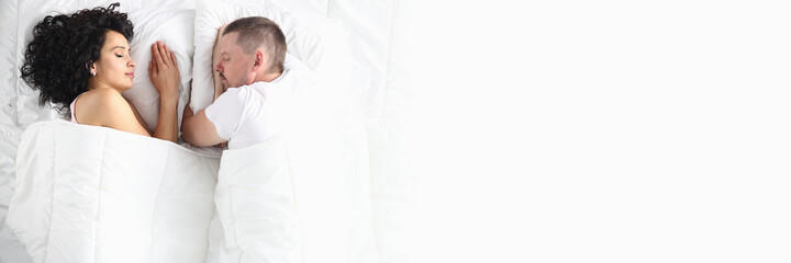 Man and woman on white bed lie with their eyes closed. Intimate relationship in couples concept