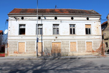 Elongated old abandoned suburban family house with boarded and broken windows on dilapidated cracked facade in old part of town on cold sunny winter day
