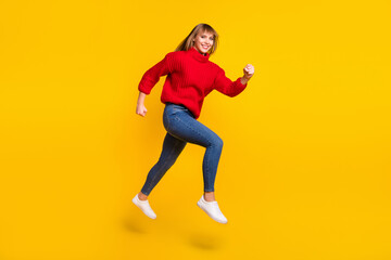 Full size profile photo of blond optimistic lady jump wear red sweater jeans sneakers isolated on bright yellow color background