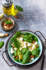 Couscous salad with pear, spinach, almonds, feta cheese and vinaigrette sauce on a gray stone table. Copy space.