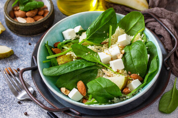 Couscous salad with pear, spinach, almonds, feta cheese and vinaigrette sauce on a gray stone table.