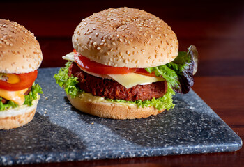 Tasty vegetarian food, homemade cheeseburgers made from plant based soya meat with cheese, onion, green lettuce and tomatoes