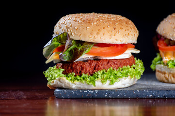 Tasty vegetarian food, homemade cheeseburgers made from plant based soya meat with cheese, onion, green lettuce and tomatoes