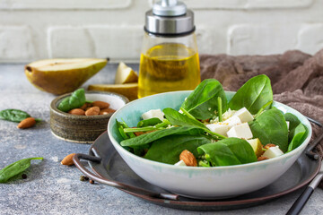 Couscous salad with pear, spinach, almonds, feta cheese and vinaigrette sauce on a gray stone table.