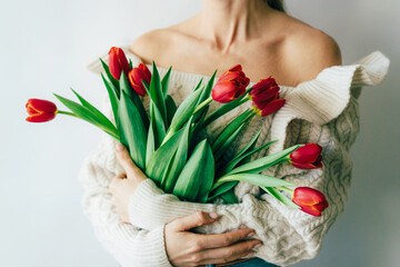 Unrecognizable woman with bare shoulders holding a bouquet of red tulips. Spring floral concept.