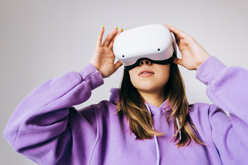 Young caucasian woman using VR headset, touching glasses and looking up in virtual reality on white background.