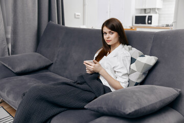 Obraz premium woman covered with a blanket sits on the couch with a phone in her hand
