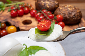 Cheese collection, eating. of white soft Italian cheese mozzarella, served with red cherry tomatoes, fresh basil leaves