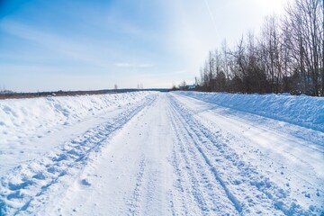Fototapeta na wymiar Rural road in winter covered with rolled snow on the background of snow-covered fields and forests with a clear sky