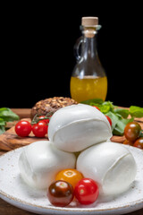 Cheese collection, white balls of soft Italian cheese mozzarella, served with red cherry tomatoes, fresh basil leaves