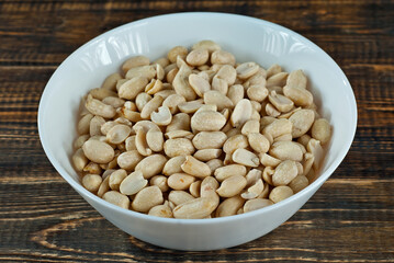 Peanuts in a white bowl on an old shabby board. Nuts on a brown wooden table.