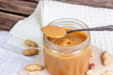 Fresh homemade crunchy peanut butter with nuts on light wooden background in the kitchen.
