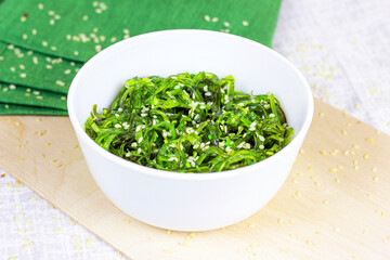Green Asian seaweed salad in a white bowl on wooden background.