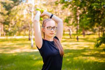 Young woman doing exercise with dumbbells. Healthy lifestyle concept. Sports training in the park.