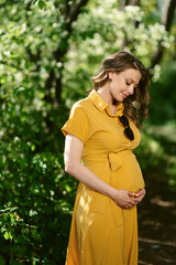 Attractive young pregnant woman in a long yellow dress outside. Warm sunny summer weather. Between...