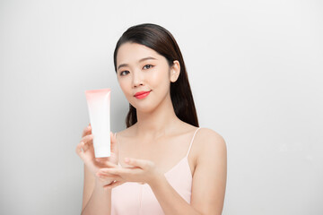 Beautiful woman shows the bottle of skincare on a gray background.