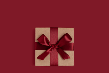 Gift box tied with ribbon on a red background. Festive minimal composition.