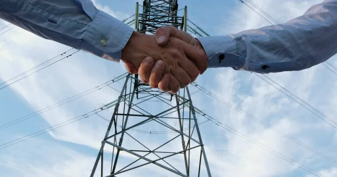 A handshake of two men in shirts against the background of a metal pole of power lines and wires.