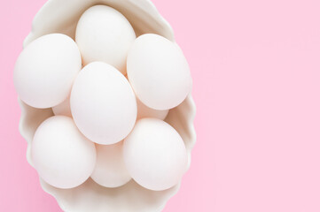Many white eggs in a white dish on a pink background. Easter. Top view
