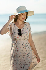 Attractive young pregnant woman in white dress and hat on the beach sea side. Expectant mother waiting for childbirth. The beginning of the third trimester of pregnancy