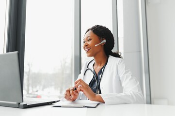 African American woman doctor working at her office online using portable inormation device....