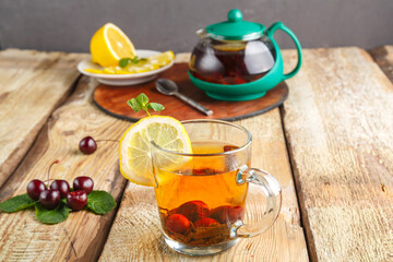 black tea in a glass cup with mint cherries and lemon on a wooden table next to fresh cherries and...