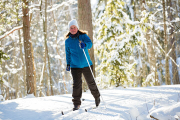 Winter sport in Finland - cross-country skiing. Pregnant woman skiing in sunny winter forest covered with snow. Active people outdoors. Scenic peaceful Finnish landscape.