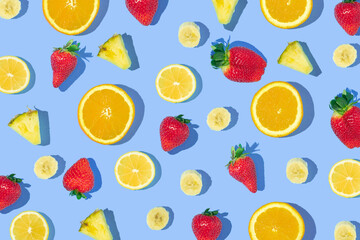 Creative pattern made with strawberries, pineapple, orange, lemon and banana slices on pastel blue background. Creative composition with fruits. Spring or summer idea.