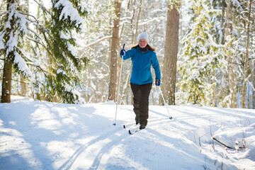 Winter sport in Finland - cross-country skiing. Pregnant woman skiing in sunny winter forest covered with snow. Active people outdoors. Scenic peaceful Finnish landscape.