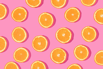 Creative pattern made with orange slices on bold pink background. Minimal flat lay. Spring or summer trendy concept. Fun idea with citrus fruits.