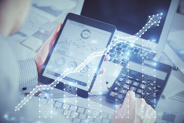 Double exposure of man's hands holding and using a digital device and forex graph drawing....