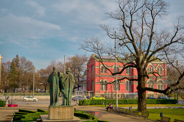 In front of Sts. Cyril and Methodius National Library with a statue and small park with dried trees and street on car. Bulgaria. Sofia. 06.01.2021.