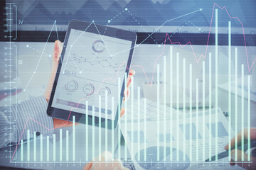 Double exposure of man's hands holding and using a digital device and forex graph drawing. Financial market concept.