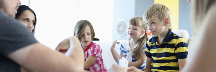 Adults and children are sitting around table on which playing cards are located boy looks thoughtfully at the adults. Board games for the whole family concept