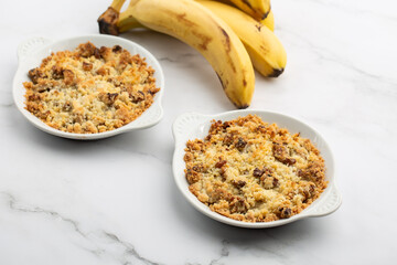 Two plates of delicious apple crumble pie isolated on marble background with bananas by side....