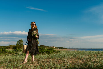 Attractive young pregnant woman in a light dress with a bouquet of flowers in her hands. Expectant mother waiting for childbirth. Between the second and third trimesters of pregnancy