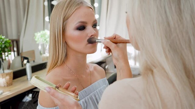 Unrecognizable makeup artist work in beauty studio. Woman applying color tone using brush