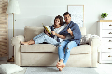 Obraz premium Happy couple covered with warm dark blue plaid reading book on sofa at home