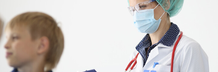 Doctor in protective medical mask writes readings on clipboard next to doctor listens with...