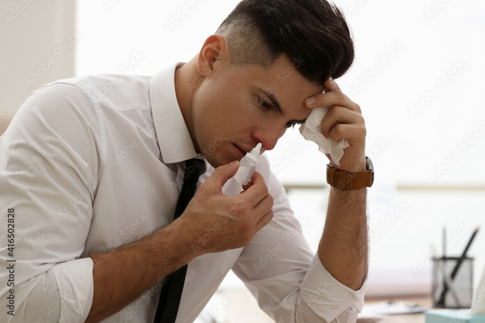 Sticker Ill businessman using nasal spray at table in office