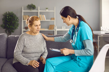 Worried mature woman sitting on sofa at home and talking to nurse or doctor. Female physician or general practitioner supporting senior patient during health consultation at modern clinic or hospital