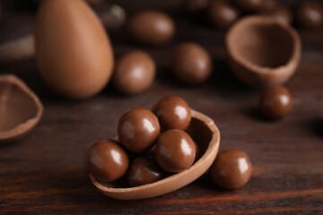 Half of tasty chocolate egg with candies on wooden table, closeup. Space for text