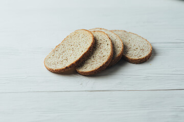 A white and silver toaster sits on a white wooden table with slices of bread next to it