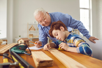 Experienced old carpenter teaching little child new handwork skills. Senior man and teen grandchild...