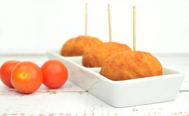 
Croquettes on a small rectangular plate. Rustic wood background, cherrys tomatoes scattered.