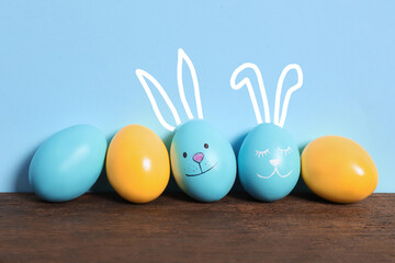 Two eggs with drawn faces and ears as Easter bunnies among others on wooden table against light blue background