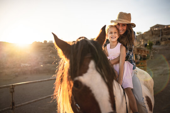 Happy mother and daughter riding a horse at sunset - Family and love concept - Focus on woman eyes