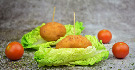 Croquettes on small leaves of tudela heart lettuce. Stone background, Cherrys tomatoes scattered.