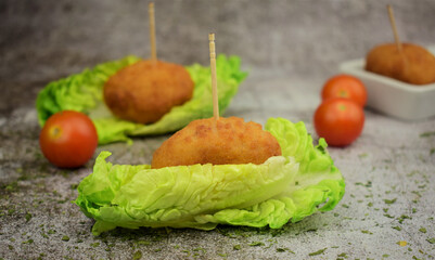 Croquettes on small leaves of tudela heart lettuce. Stone background, cherrys tomatoes scattered.